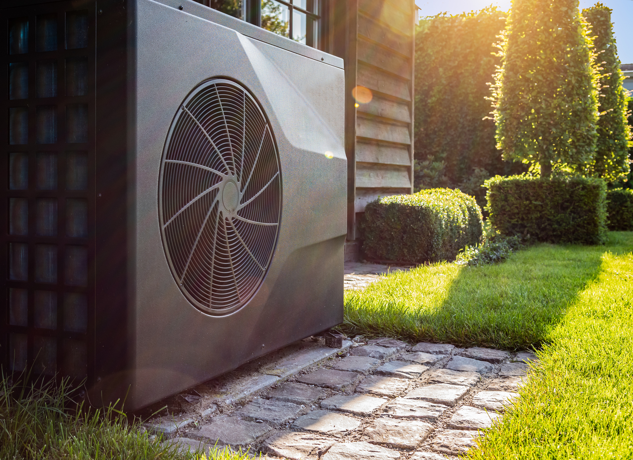 Outdoor residential AC unit beside a home on a sunny summer day, representing peak electrical demand on home panels and circuits.