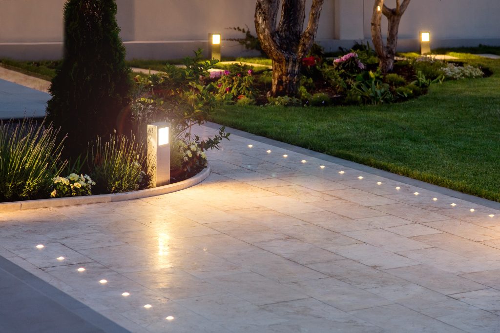 Marble tile driveway with landscape lighting illuminating flowerbeds and lawn at dusk in Cincinnati.