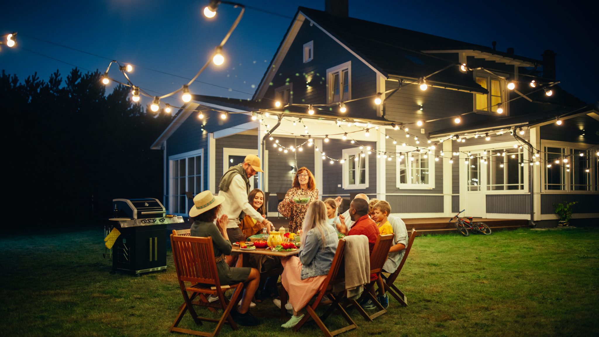 Family and friends enjoying an outdoor dinner party under patio lighting on a warm Cincinnati summer evening.