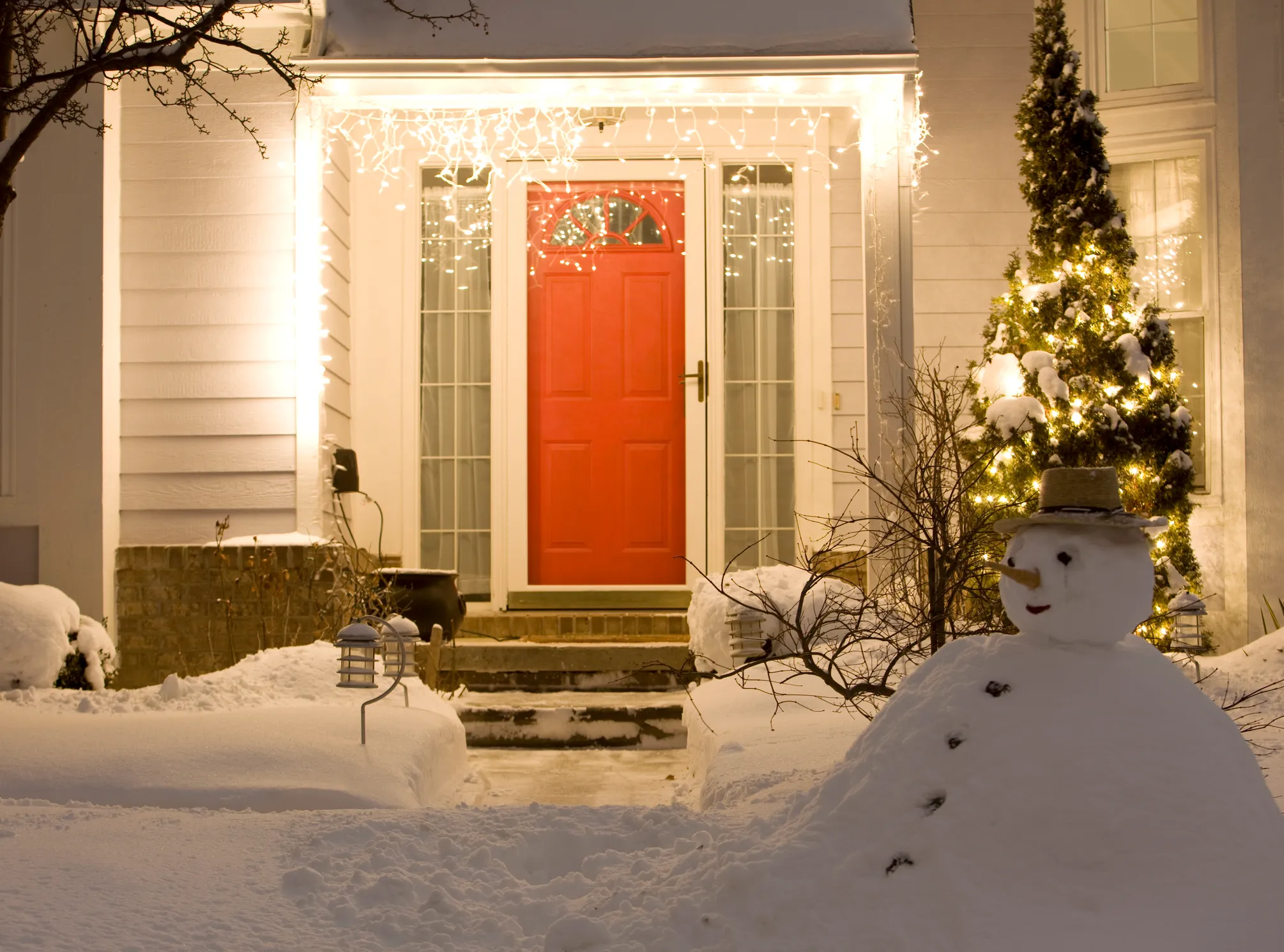 Snowy front yard and porch glowing with Christmas lights at night, showing a home kept powered by winter generator prep